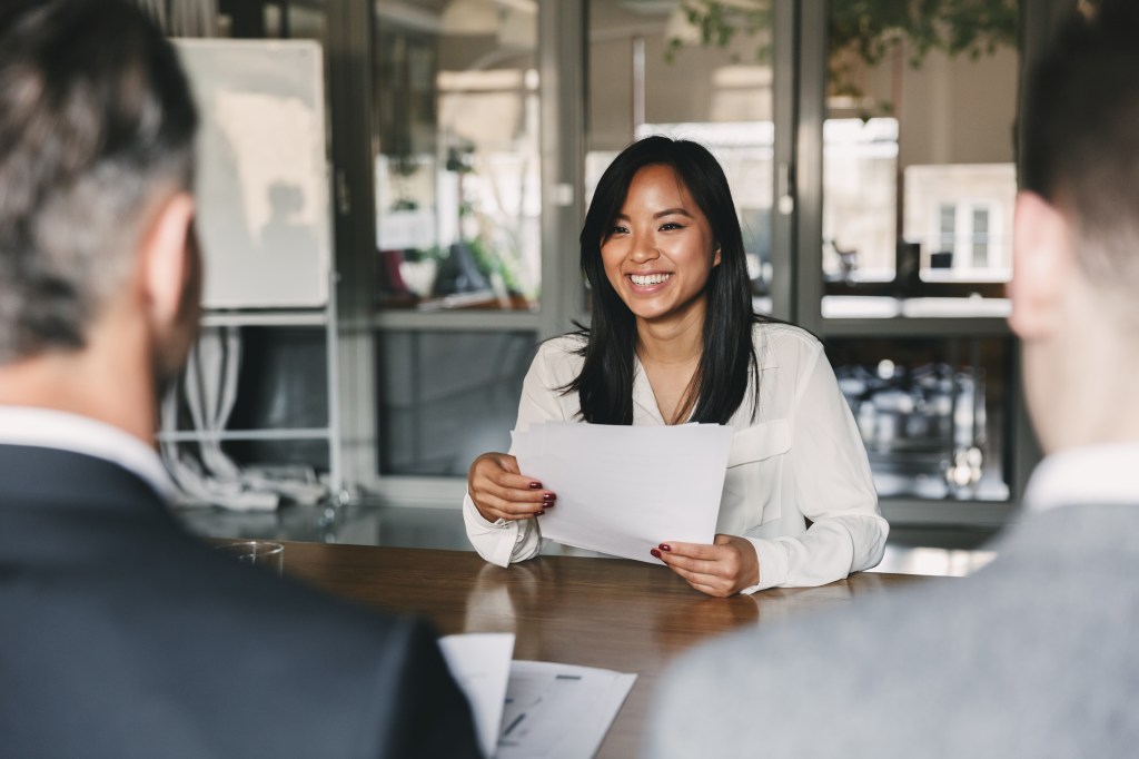 Young Asian woman smiling and holding a resume during a corporate meeting or job interview